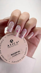 Hand with floral nail design holding a container of Atica Professional builder gel.