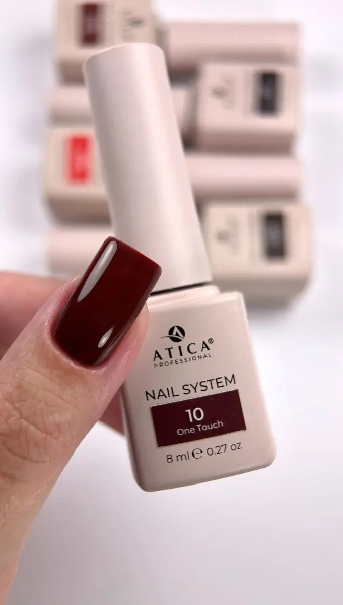 A hand holding an 8ml bottle of ATICA Professional Nail System shade 10 'One Touch' in a deep burgundy color, with other bottles blurred in the background.