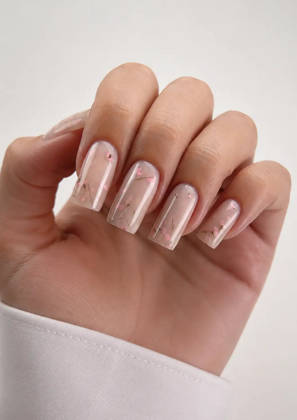 Hand with transparent nail polish and small floral designs on a light background