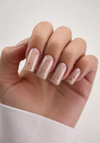 Hand with transparent nail polish and small floral designs on a light background