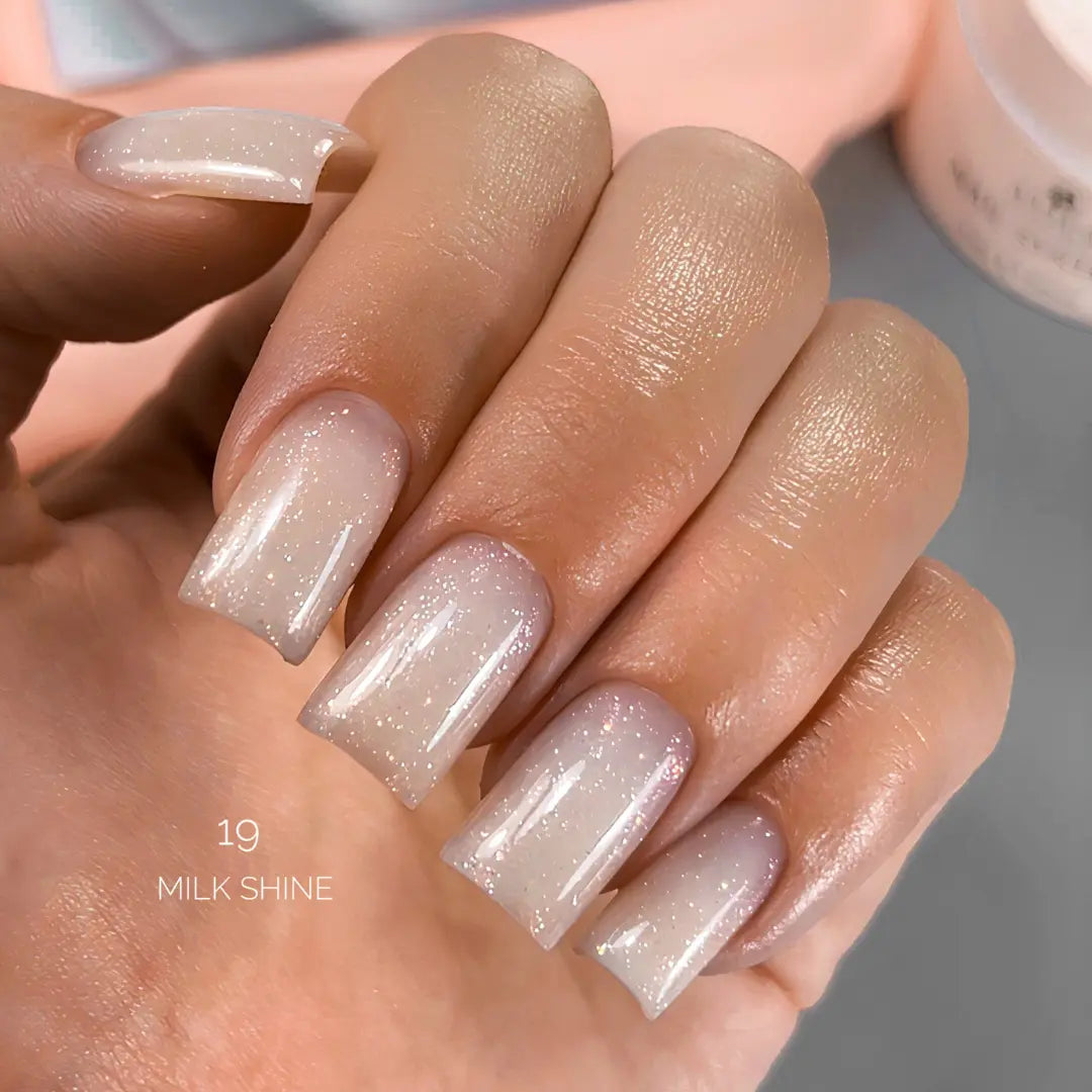 Close-up of a hand with beige and glittery nails, labeled 'Milk Shine'.