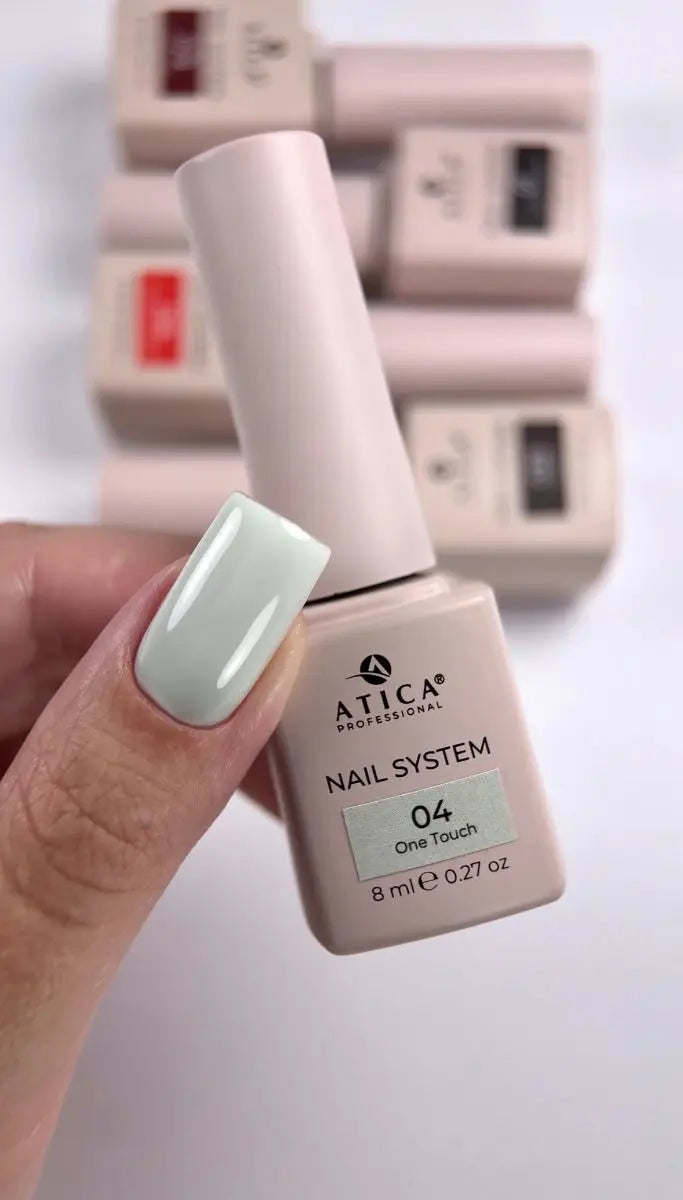 A hand with a light mint green manicured fingernail holds an ATICA Professional nail system bottle labeled shade 04 One Touch. The bottle is a pale pinkish-beige color, with other matching bottles blurred in the background.