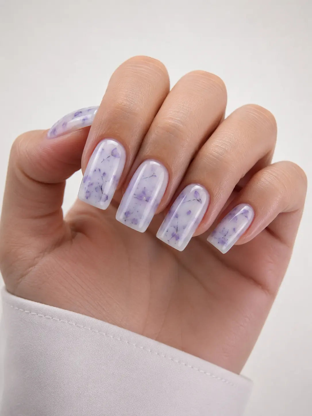 Hand with clear nail polish and purple floral designs on a white background