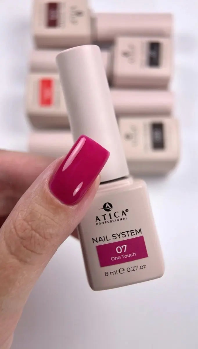 A hand with bright magenta nail polish holds an ATICA Professional nail system bottle labeled shade 07 One Touch. Other ATICA bottles are blurred in the background on a white surface.