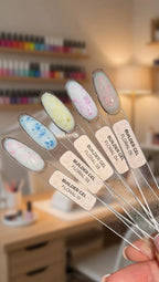 Set of Builder Gel applicators with colorful designs held by a hand, blurred background of nail polish bottles.