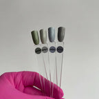 Four test tubes with green and gray lids held by a pink-gloved hand against a plain background