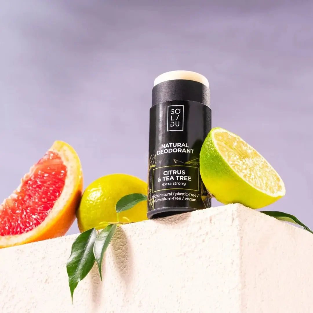 Solidu natural deodorant stick with citrus and tea tree scents on a white towel with fruits.