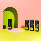 Four black cylindrical containers with green labels on a pink and yellow background