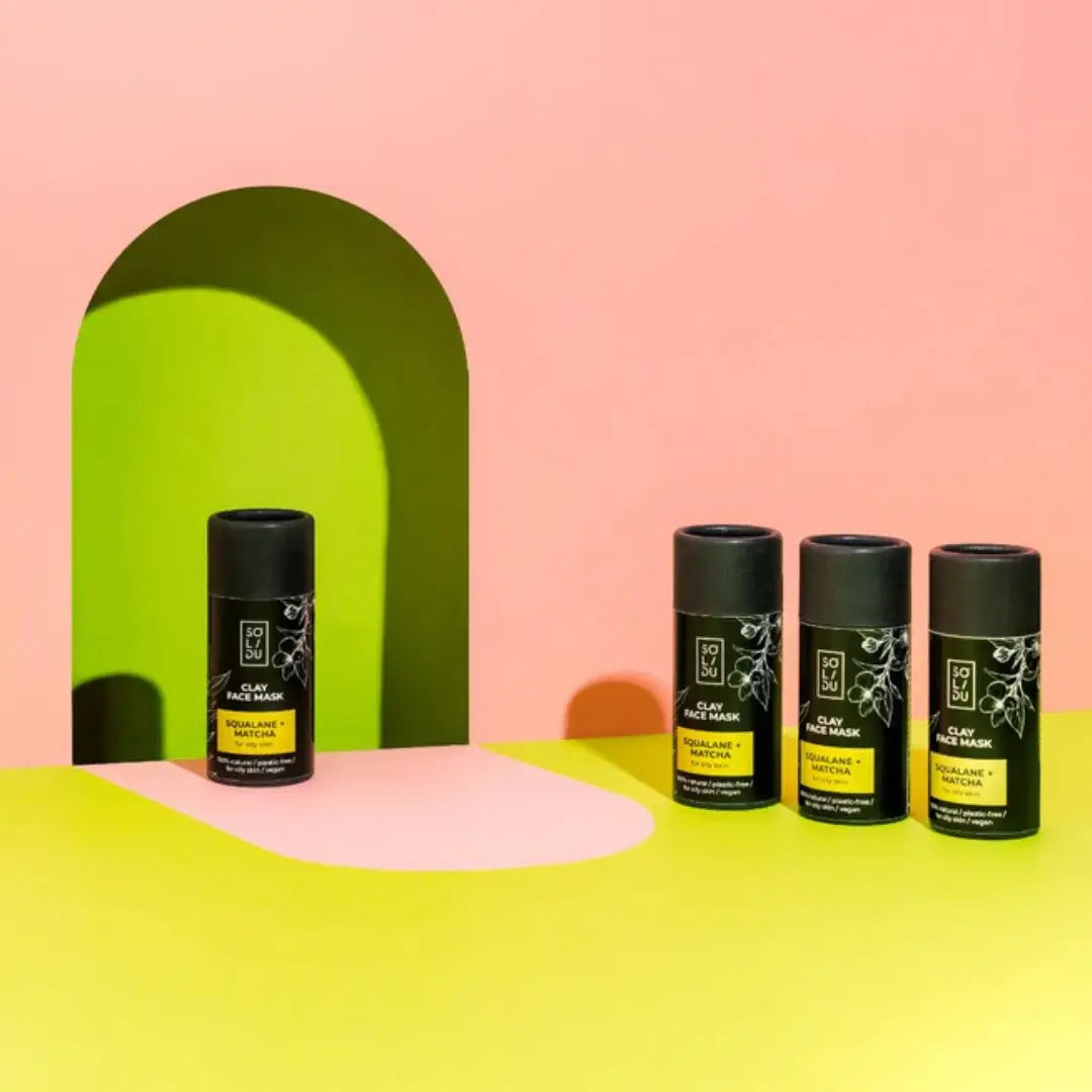 Four black cylindrical containers with green labels on a pink and yellow background