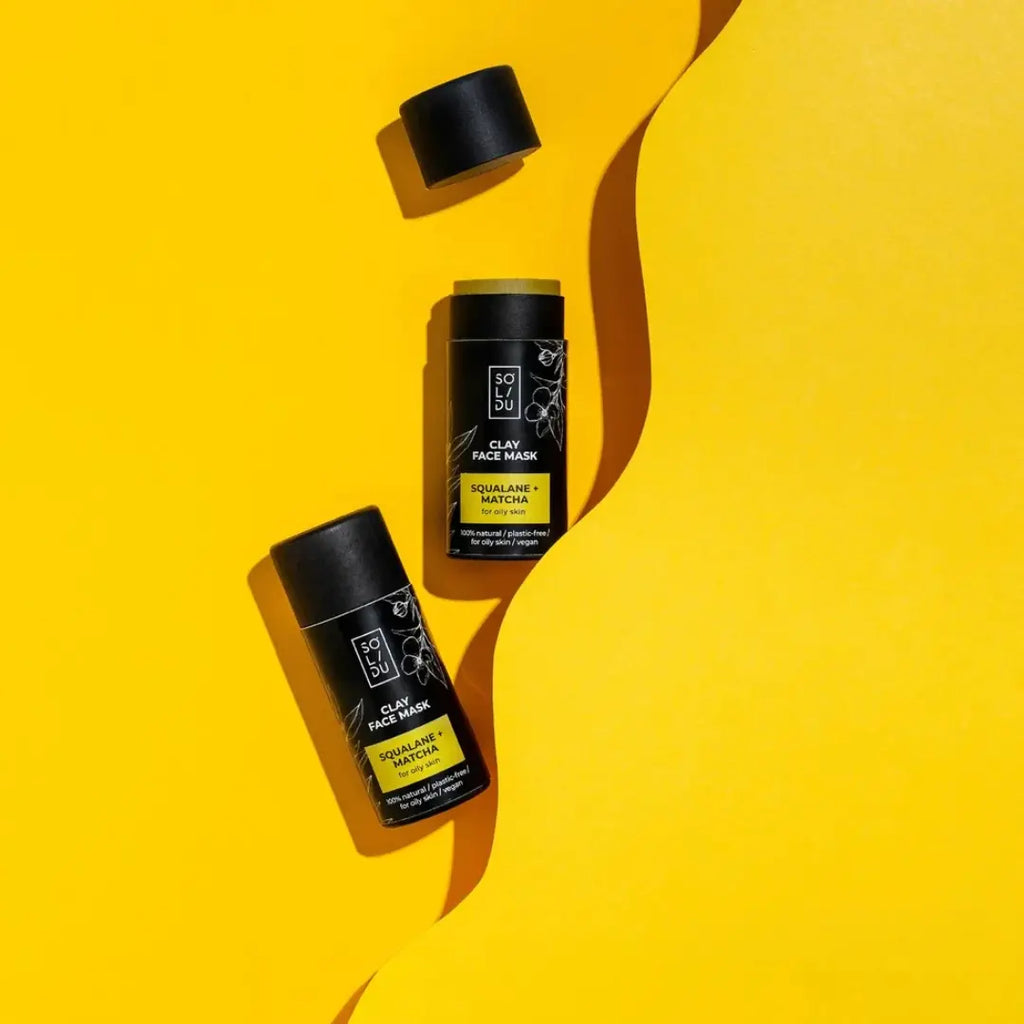 Two black face mask containers with yellow labels on a yellow background