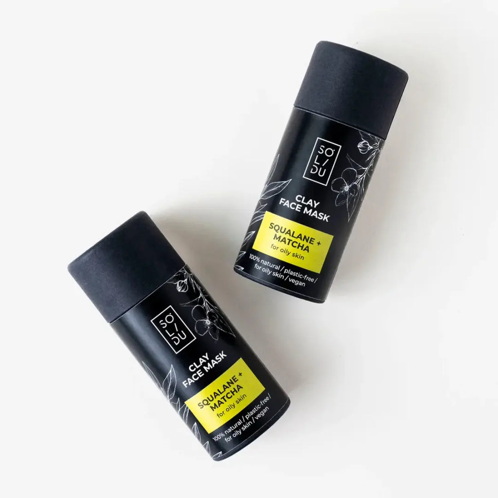 Two black clay face mask containers with yellow labels on a white background