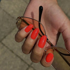 I Don’t Care bright coral-red gel nail polish on oval-shaped nails holding sunglasses