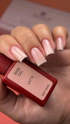 Hand with pink nail polish holding a bottle labeled 'Base Gel Latte' on a blurred background