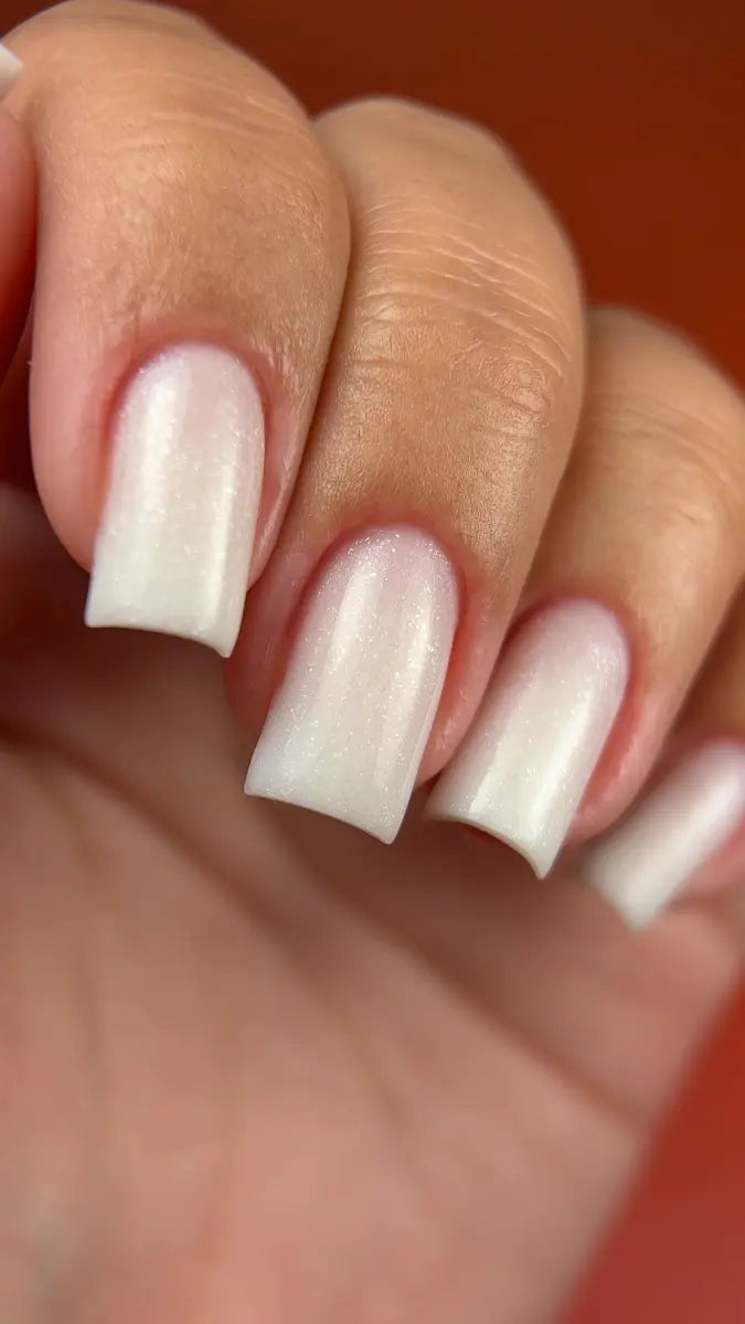 Close-up of a hand with white nail polish on a blurred background