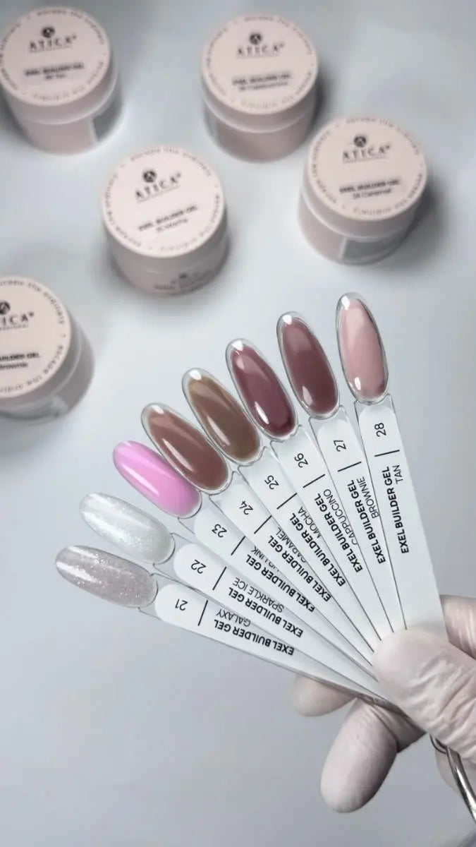 A hand wearing a white glove holds a fan of nail gel color swatch sticks showing various shades, with multiple small jars of ATECA gel polish powder in the background on a light gray surface.