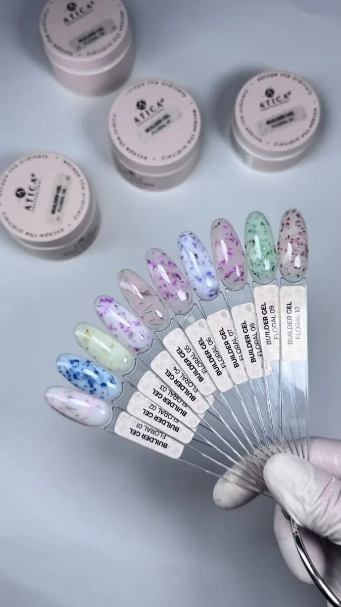 A hand wearing a white glove holds a fan of nail polish sample sticks showing various glitter and speckle shades, with several small jars of gel polish in the background. The brand name 'ALICA' is visible on the jars and labels.