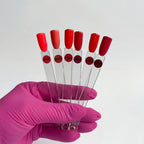 Hand holding six test tubes with red caps and labels, against a white background