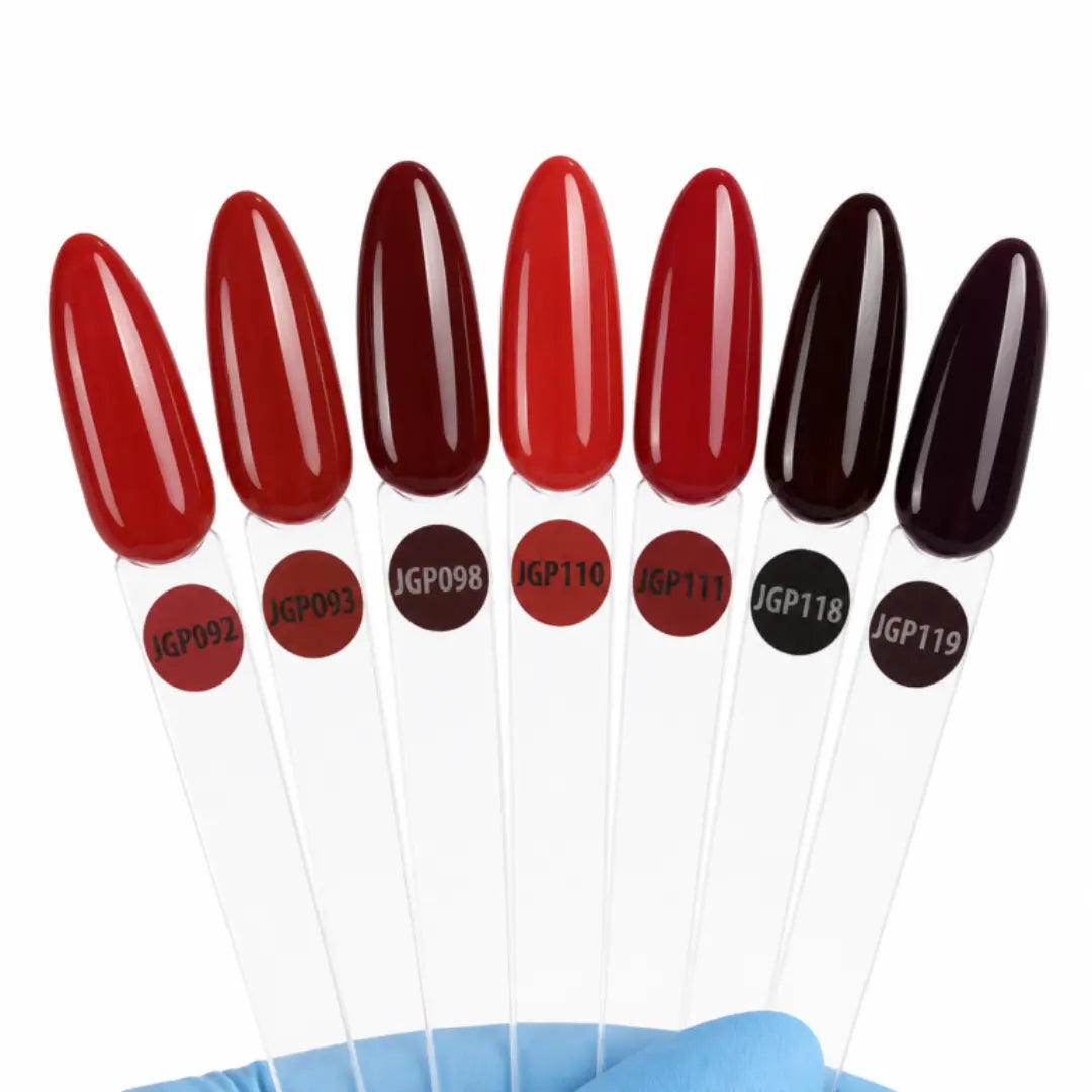 Seven glossy nail color swatches on clear plastic sticks, each labeled with a shade code, held against a white background with a blue gloved hand at the bottom.