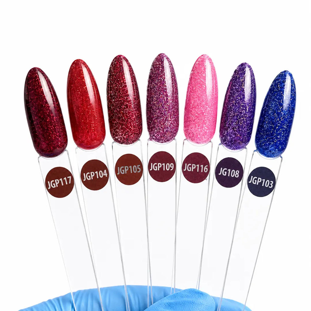 Eight nail polish color swatches on clear plastic sticks, each topped with an elongated nail-shaped sample and labeled with codes such as JGP117, JGP104, JGP105, JGP109, JGP116, JGP108, JGP103. A blue gloved hand is visible at the bottom holding the swatches against a plain white background.