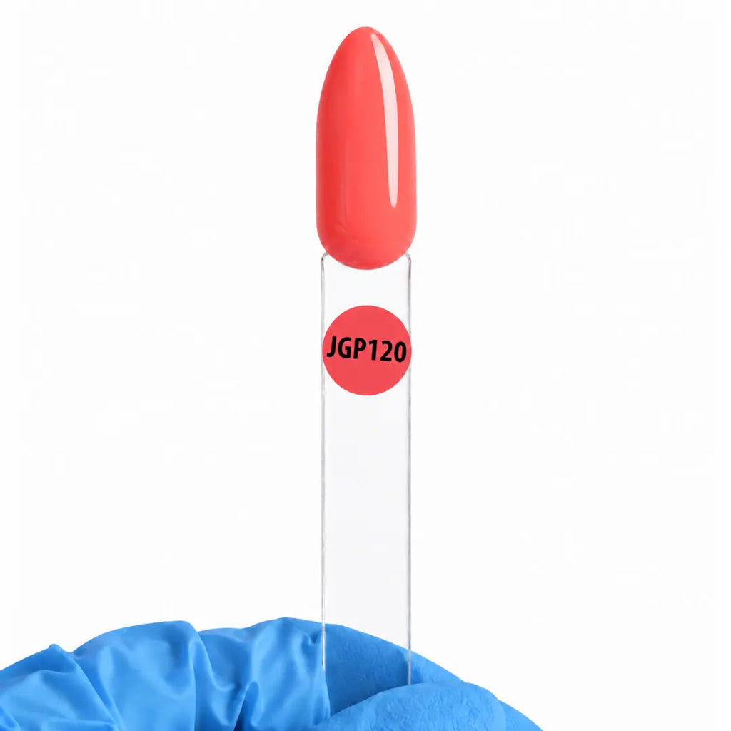 A clear nail sample tube with a glossy red cap showing a coral-red nail polish color, labeled 'JGP120' in black text on a red circle. The tube is set in a blue fabric holder against a plain white background.