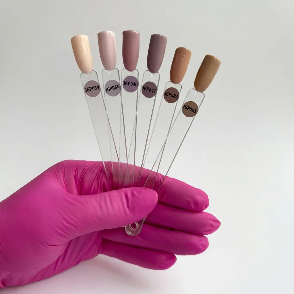 Hand holding six clear nail polish bottles with color samples against a white background