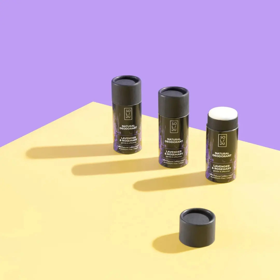 Three natural deodorant sticks on a yellow surface with a purple background