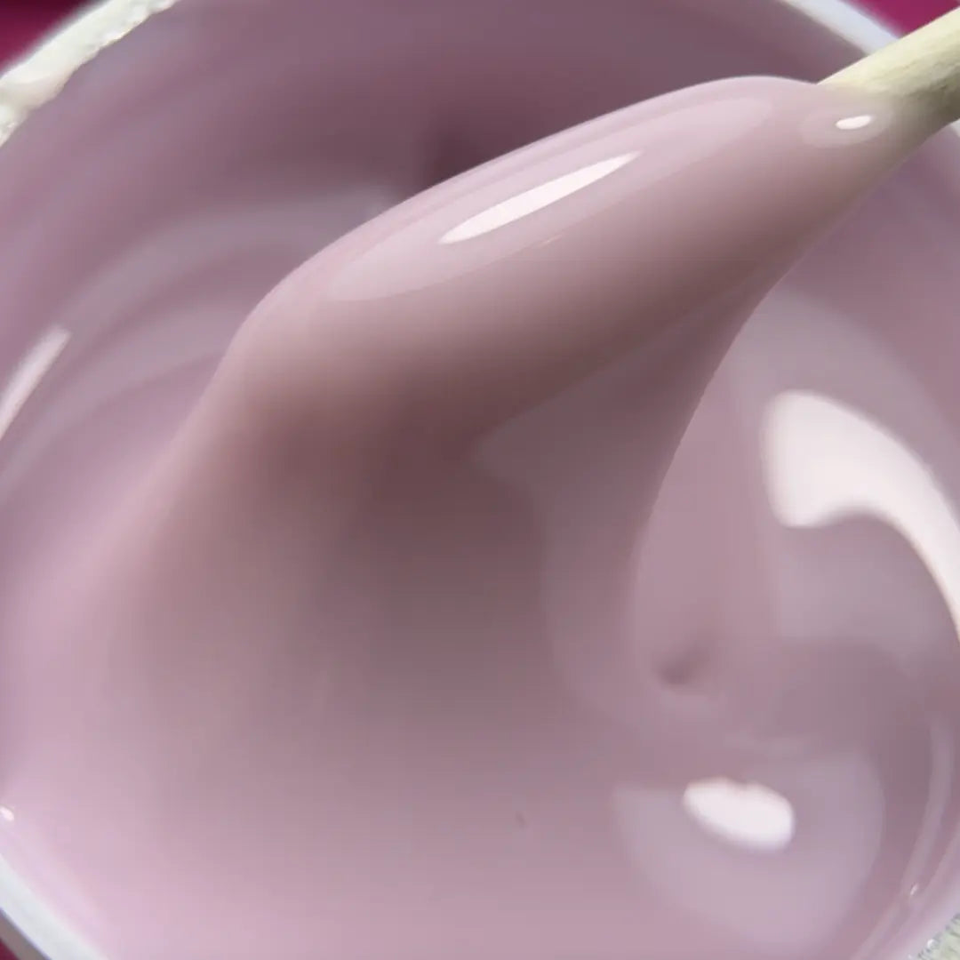 A close-up of glossy light pink gel being lifted by a wooden stick