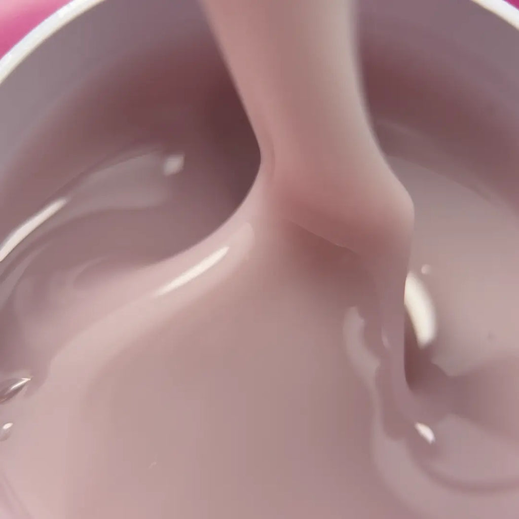 A close-up of a thick, glossy, dusty pink liquid being poured or stirred inside a container.