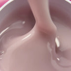 A close-up of a thick, glossy, dusty pink liquid being poured or stirred inside a container.