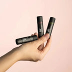 Hand holding three lip balm tubes with visible branding on a pink background