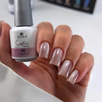Hand holding a bottle of Atica Satin nail polish with a matching manicure.