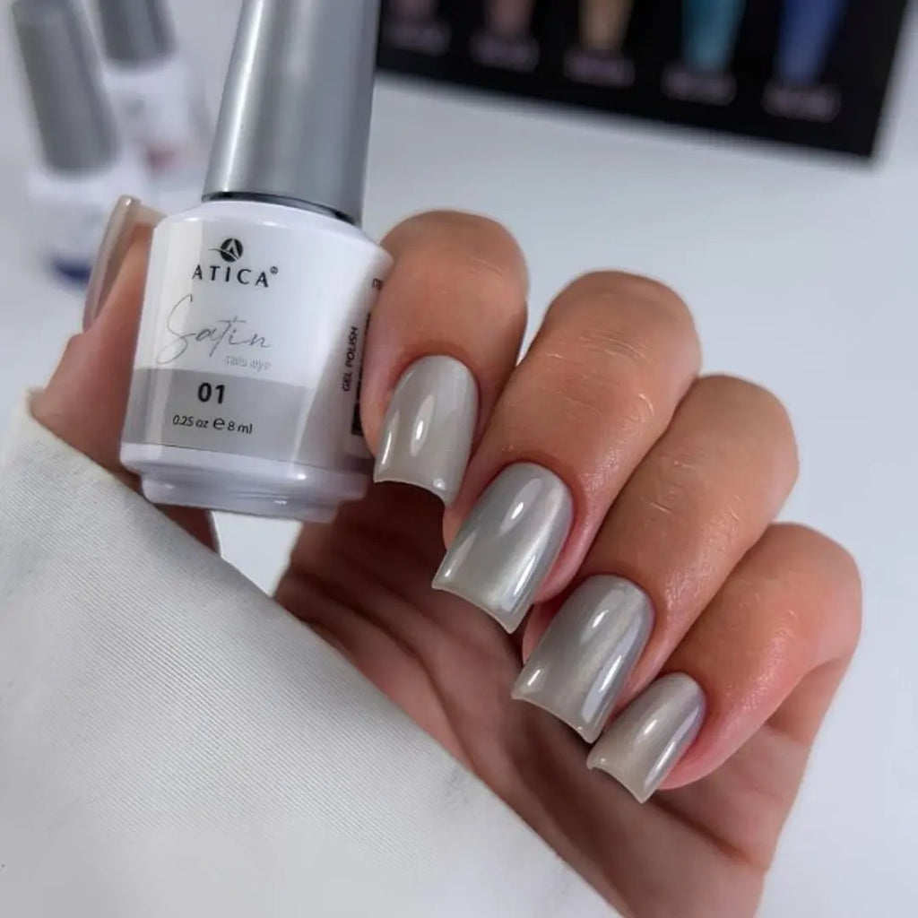Hand with gray nail polish holding a bottle of Atica Satin nail polish.