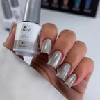 Hand with gray nail polish holding a bottle of Atica Satin nail polish.