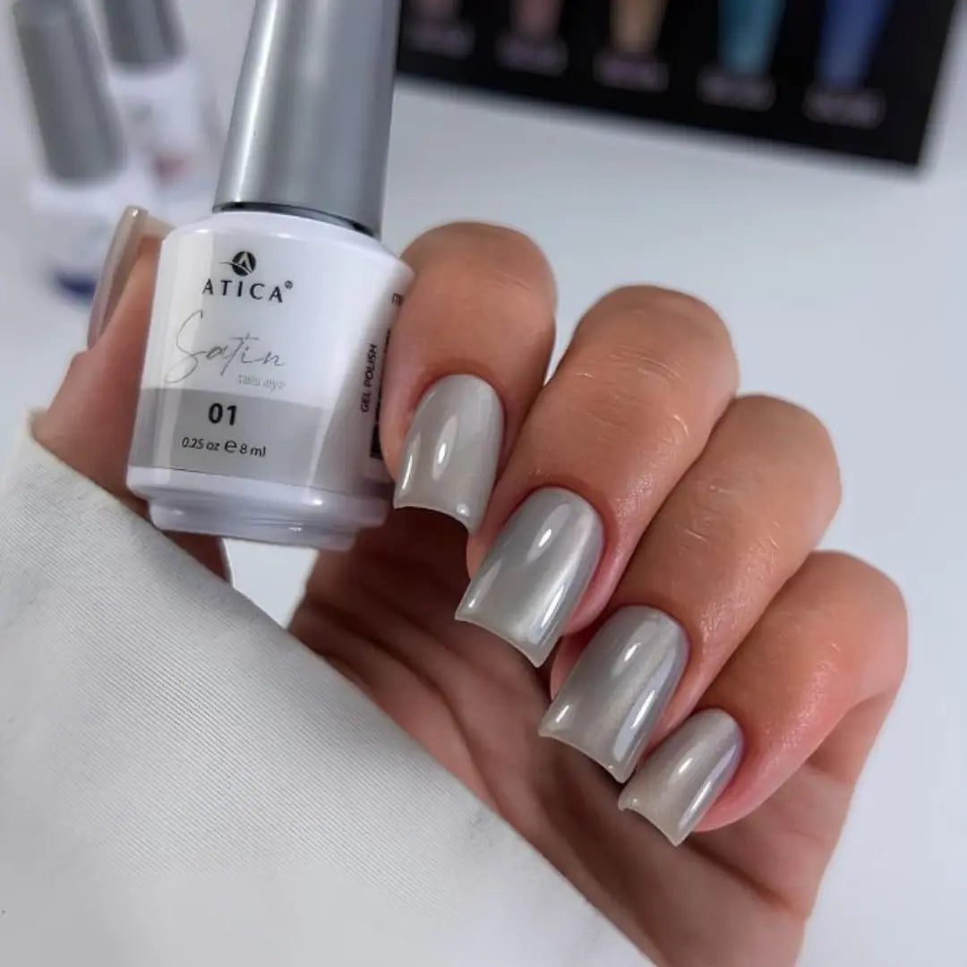 Hand with gray nail polish holding a bottle of Atica Satin nail polish.