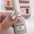 A close-up of a hand with a glossy metallic silver nail polish swatch, holding an ATICA Professional nail system bottle labeled '015 Satin White' against a soft white background with other bottles blurred behind.