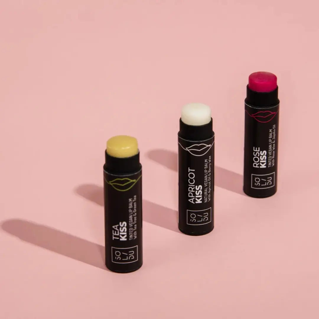 Three lip balm sticks with visible branding on a pink background
