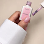 A hand holding a bottle of top gel nail polish labeled 'TOP GEL NATURAL' with a brush applicator showing the glossy light pink polish, against a plain beige background.